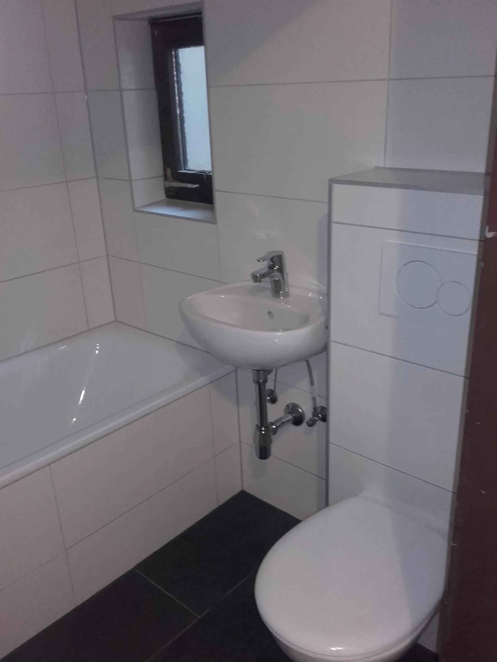 Fertiges Badezimmer mit Badewanne, Waschbecken und Wand-WC, weiß gefliest
