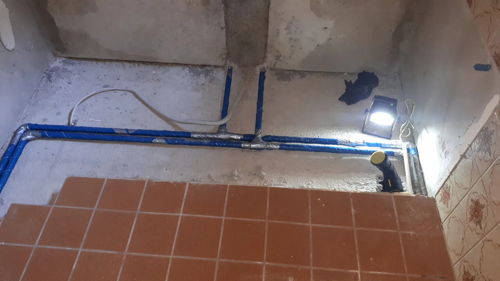 Rohinstallation im Rohbau: blau isolierte Leitungen an der Wand, daneben eine Baustellenlampe